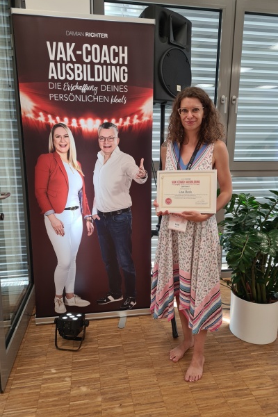 Frau mit Coaching Zertifikat in der Hand vor Banner